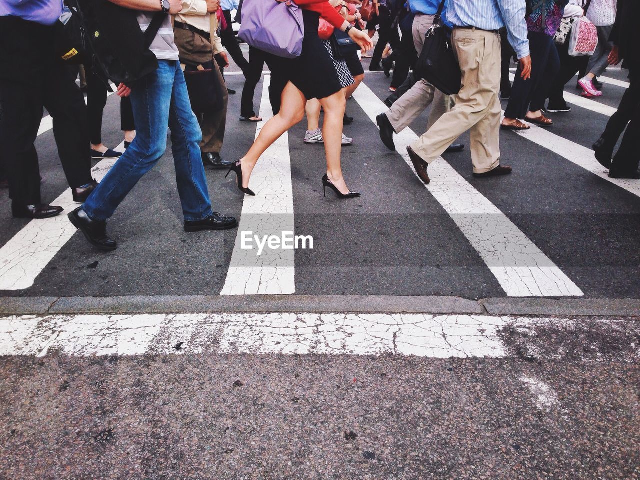 Low section of people walking on pedestrian crossing on street in city