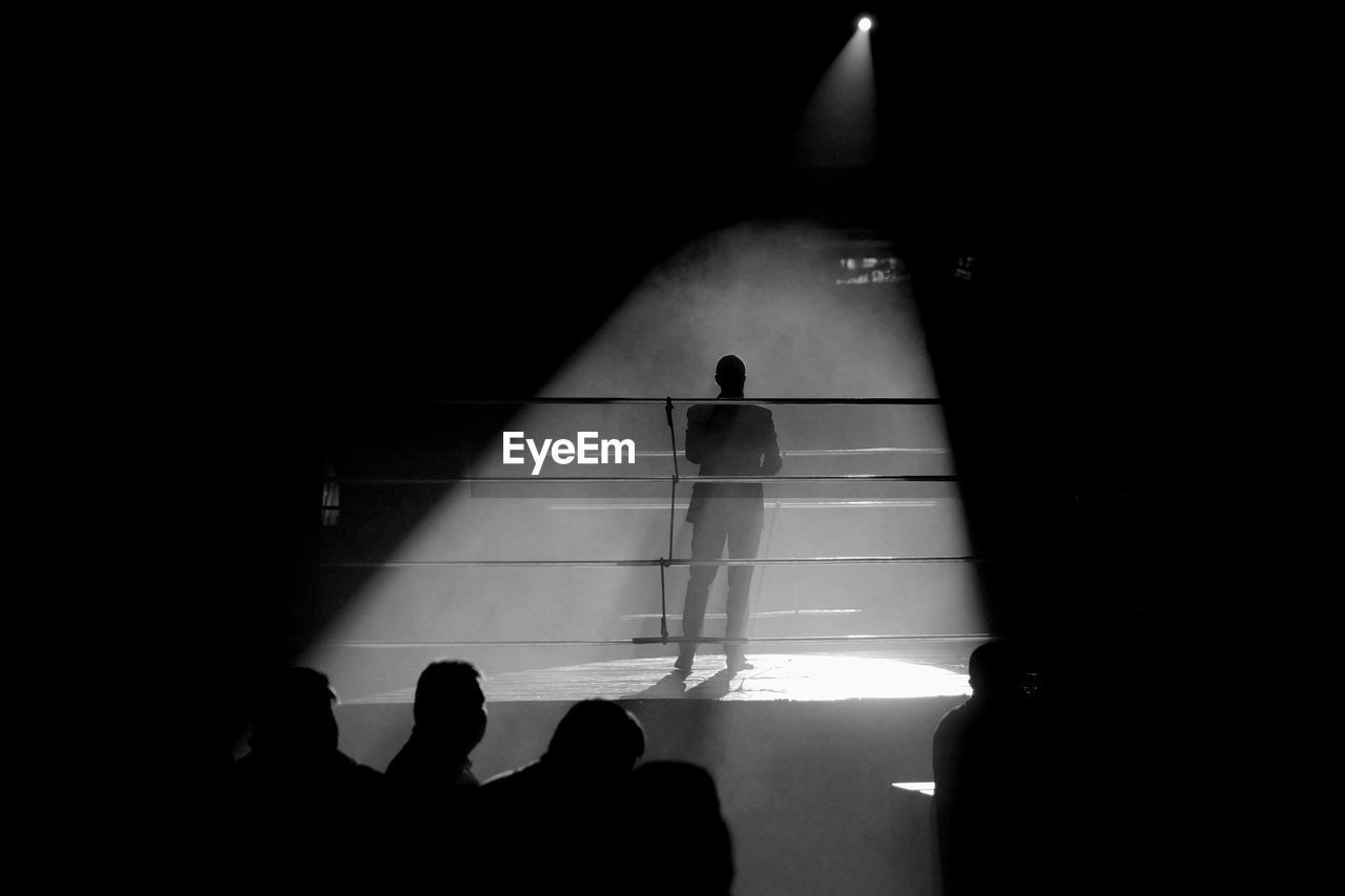 Rear view silhouette of man standing in boxing ring under spotlight