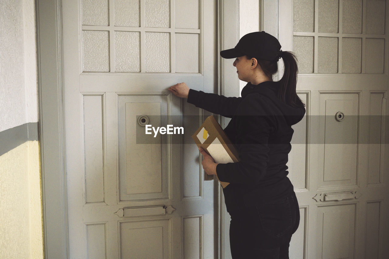 Side view of delivery woman with package knocking at door