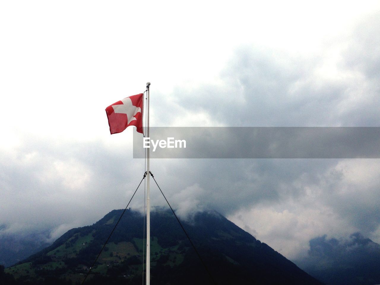 Swiss flag on mountain against cloudy sky