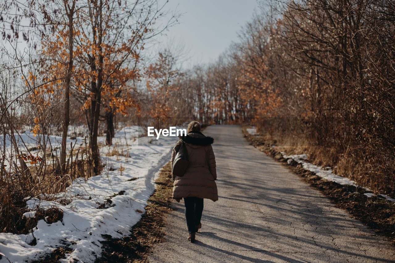 Rear view of woman walking on snow covered footpath