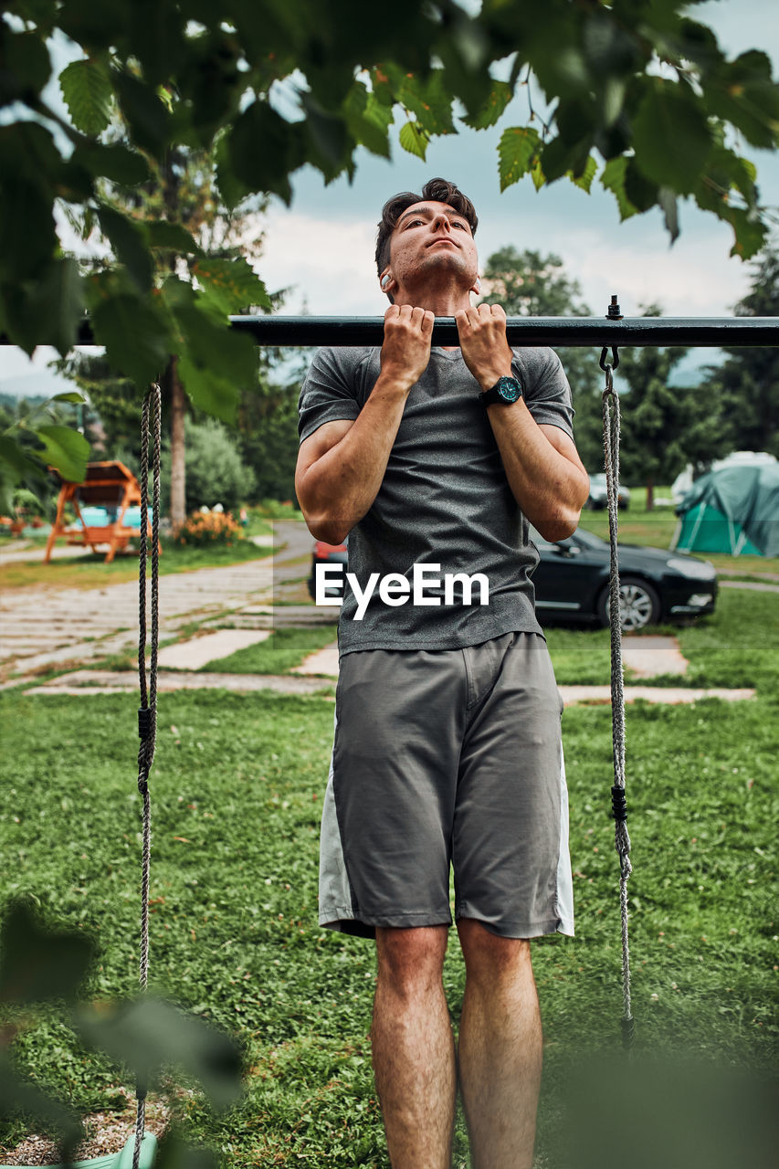 Young man doing pull-ups on pull-up horizontal bar during his calisthenics workout on a camping