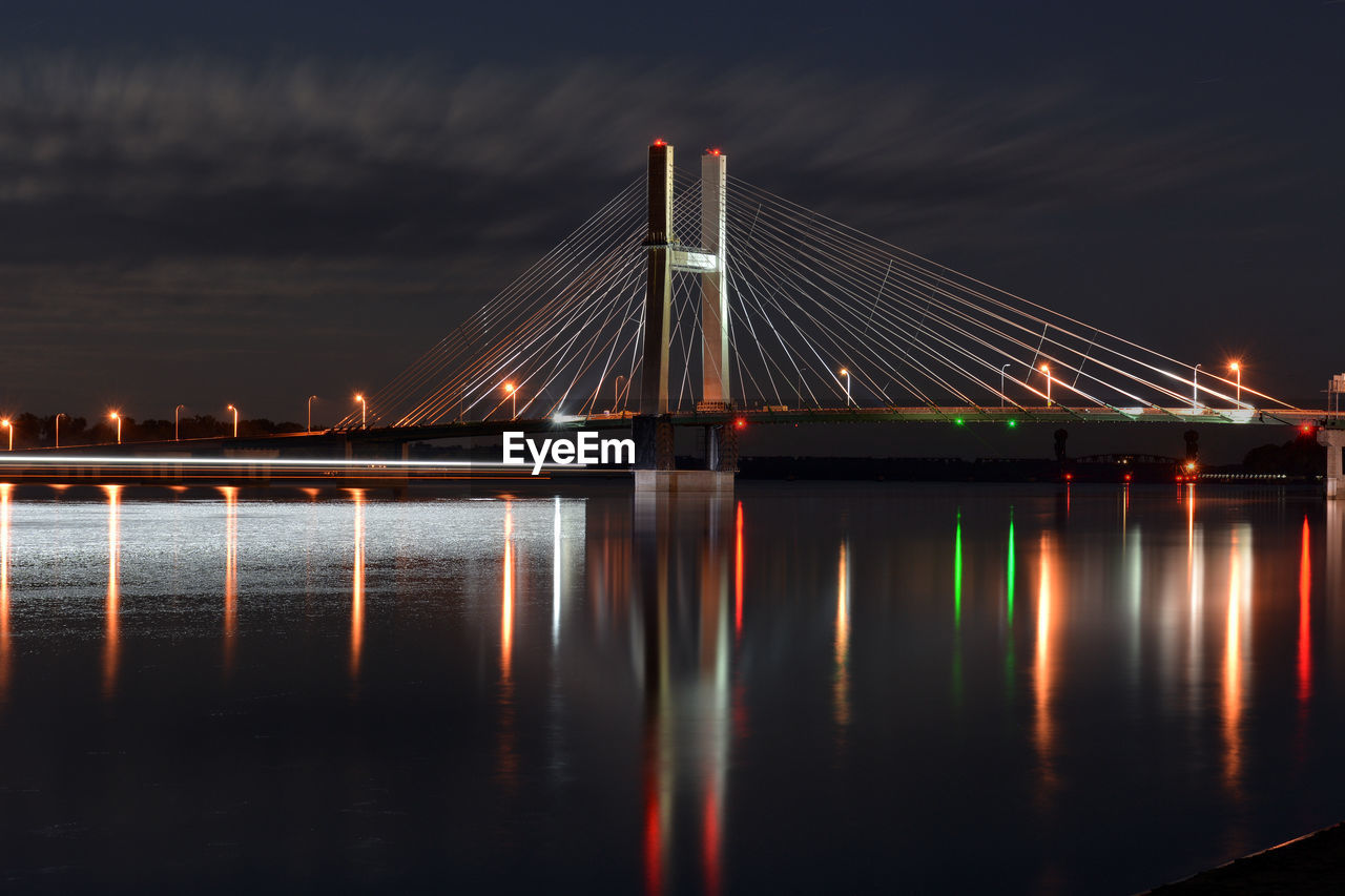 Illuminated cable-stayed bridge over river against sky at night