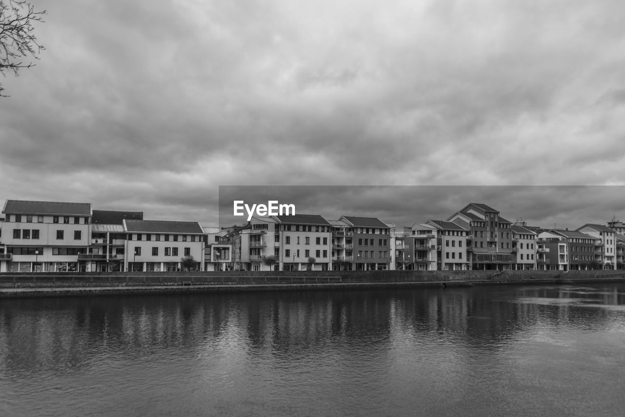 buildings in river against cloudy sky