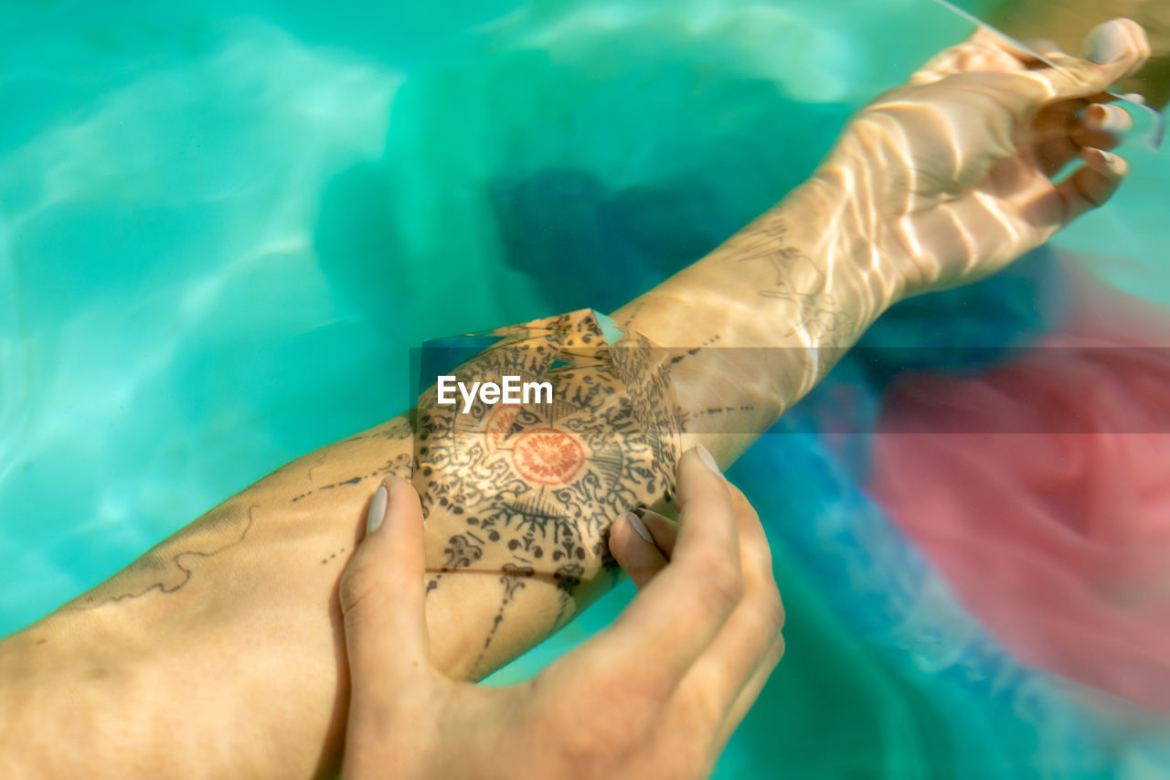Cropped image of woman with prism on tattoo underwater