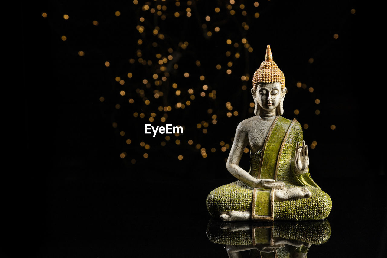 Buddha statue in meditation with lights on black background with copy space.
