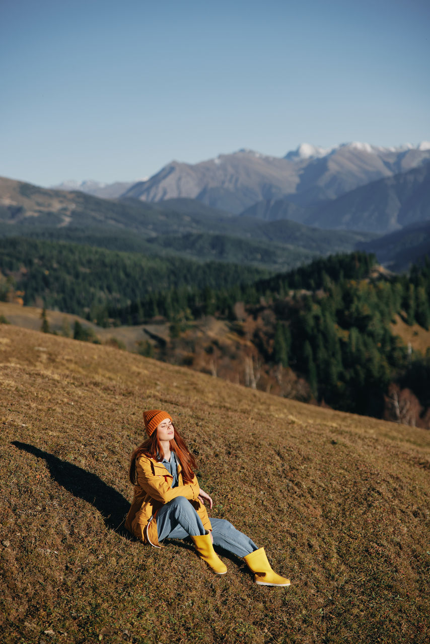 side view of woman sitting on mountain against sky