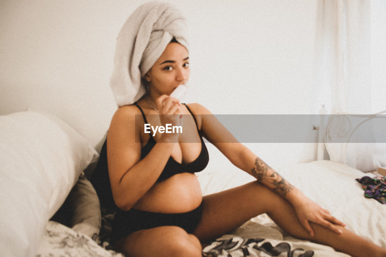 Portrait of pregnant woman in bikini sitting on bed at home