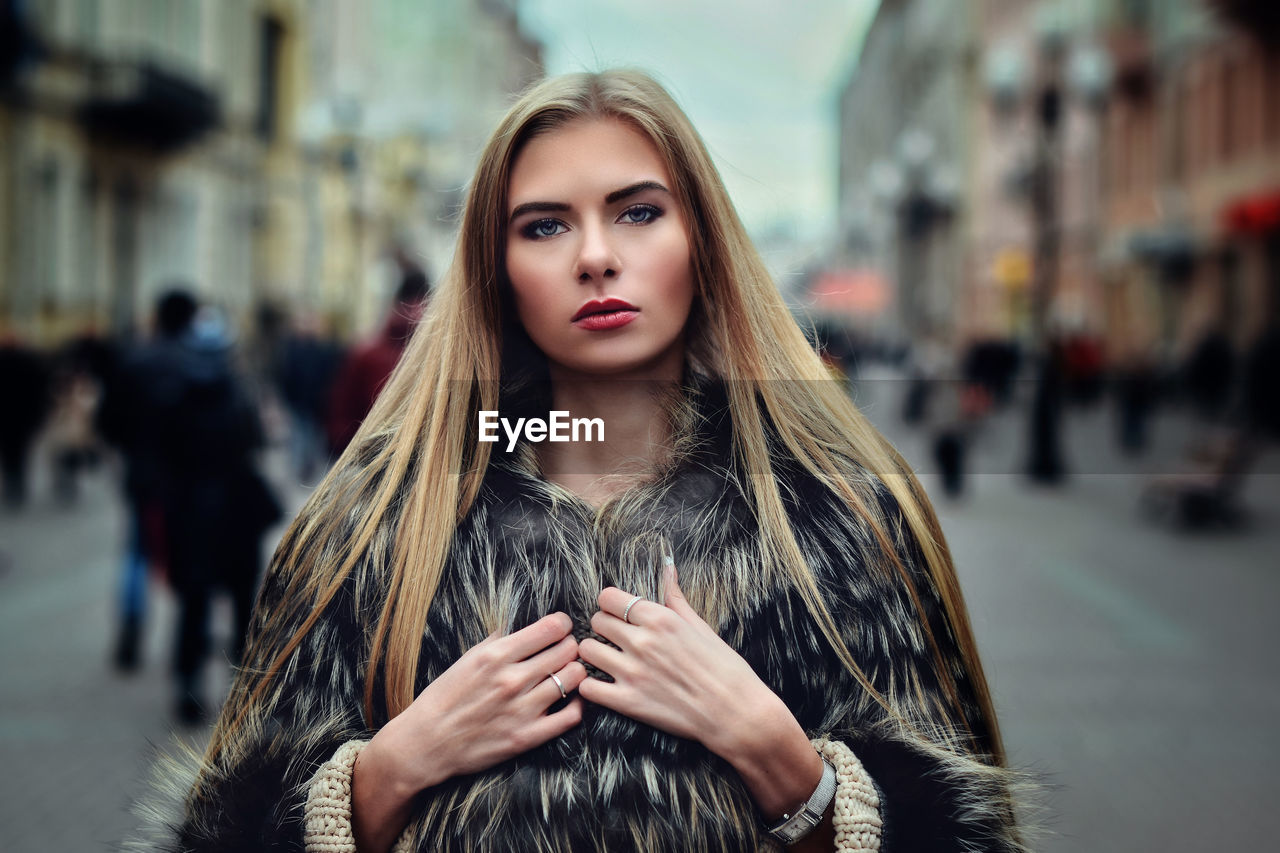 Portrait of beautiful young woman wearing fur coat on city street