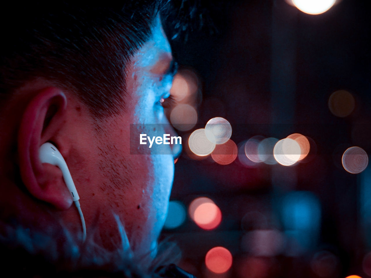 Close-up of man listening music through in-ear headphones at night