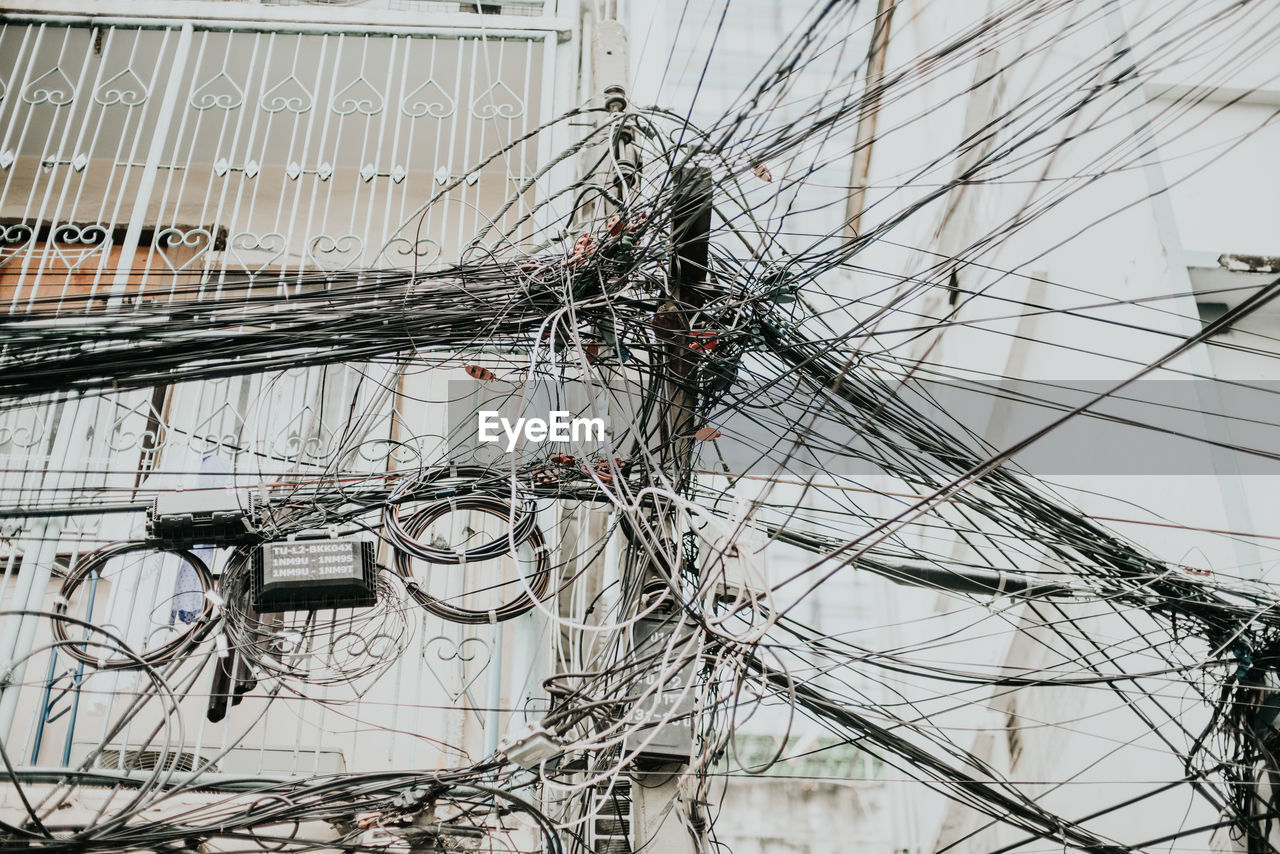 Low angle view of electricity pylon with tangled cables against building