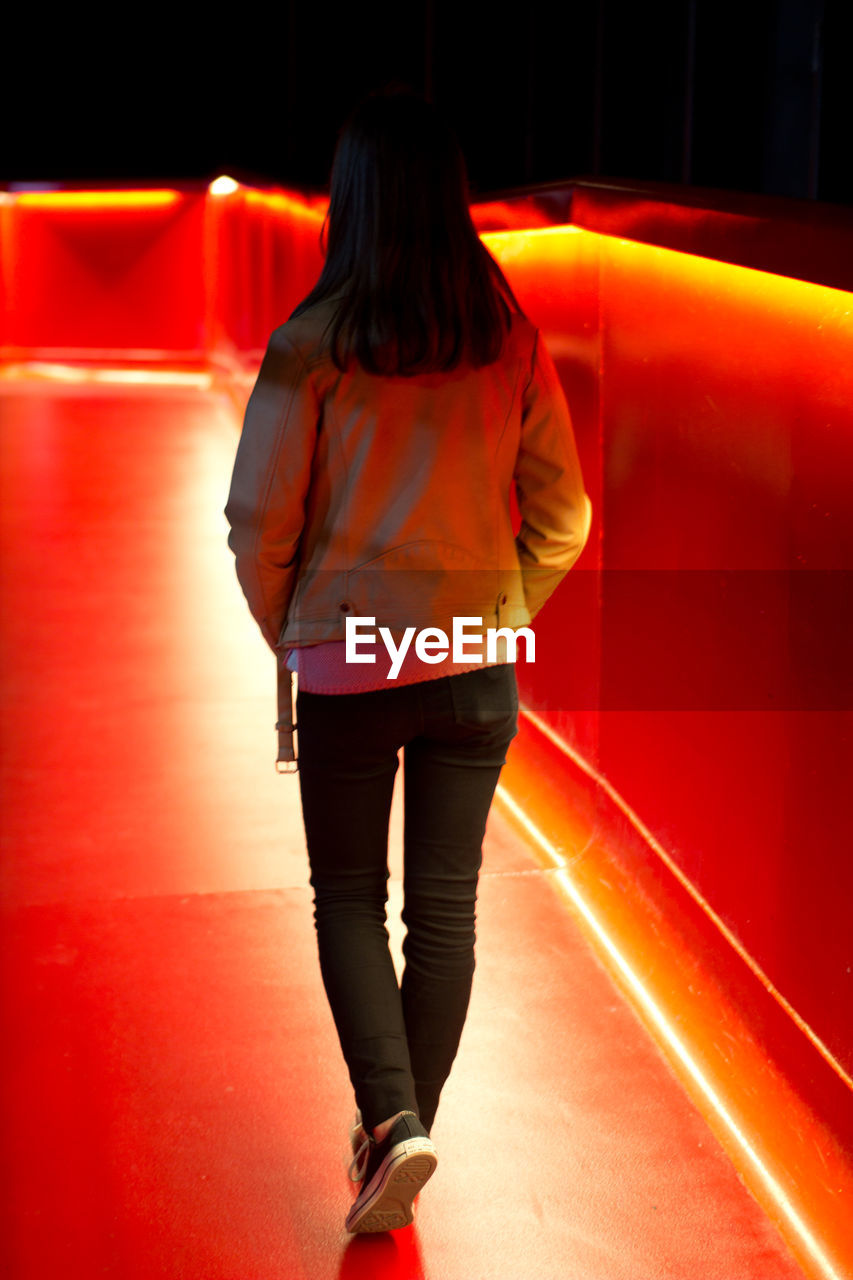 Rear view of girl walking red illuminated floor