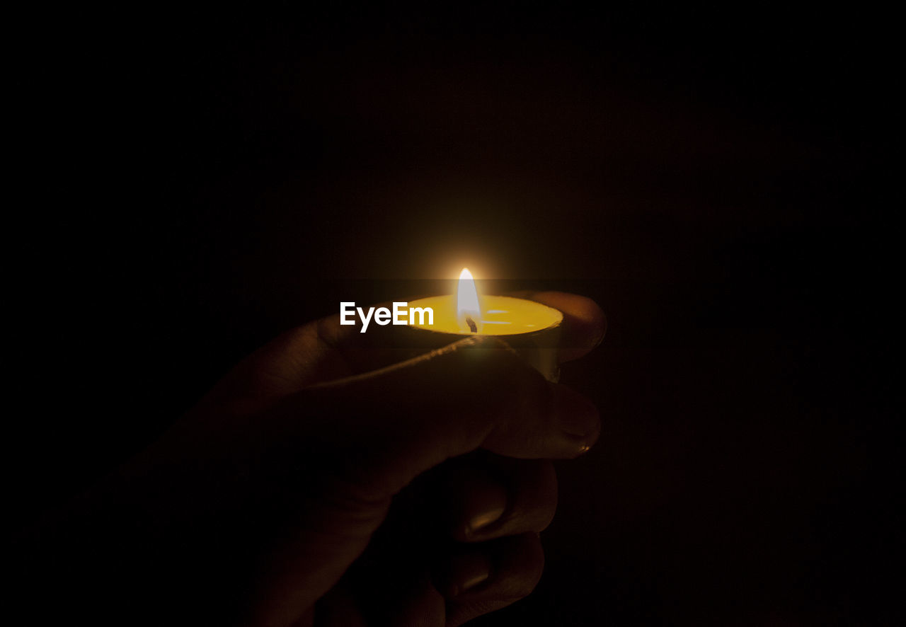 CLOSE-UP OF HAND HOLDING LIT CANDLES IN DARKROOM