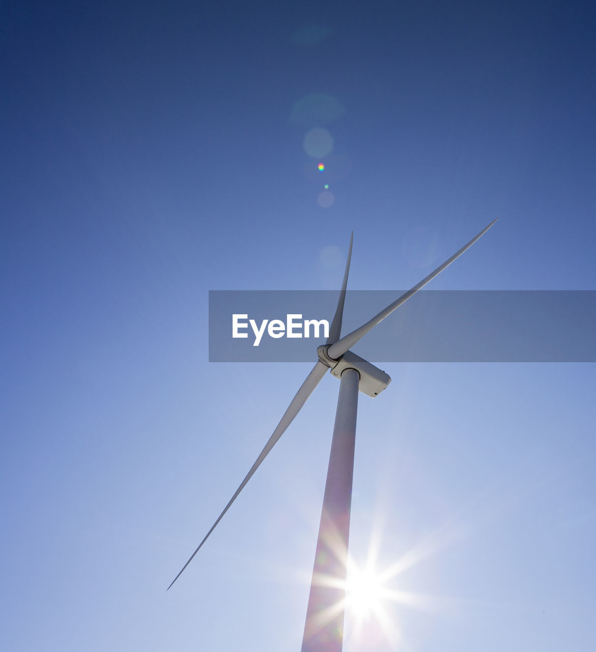 Wind turbines against blue sky with sun flare