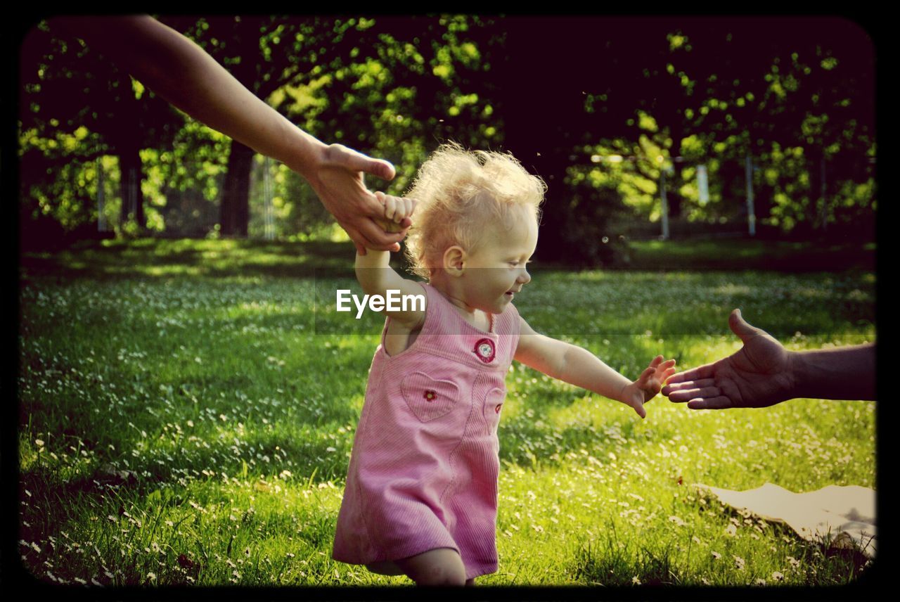 Girl holding hands of parents in park