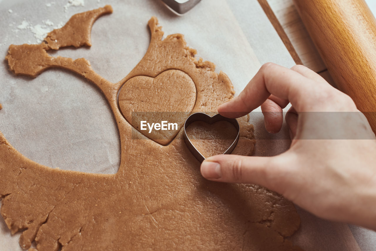 Making gingerbread cookies in shape of a heart for valentines day. woman hand use cookie cutter.