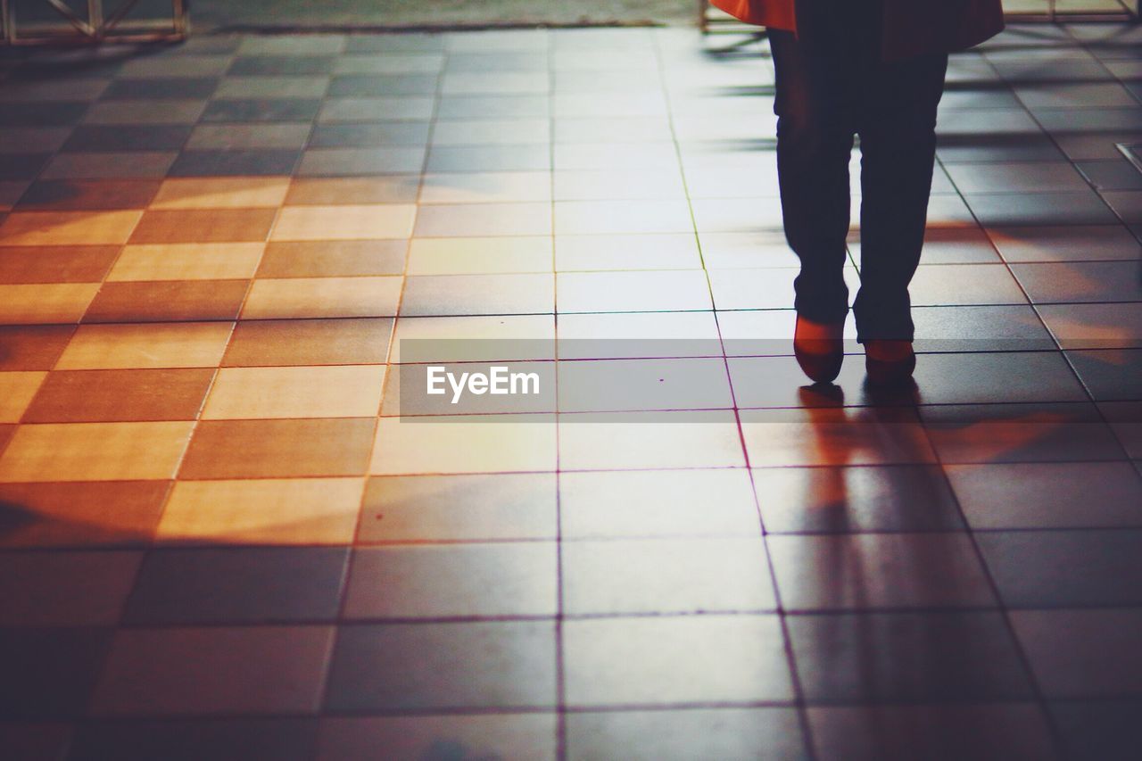 LOW SECTION OF WOMAN STANDING ON TILED FLOOR