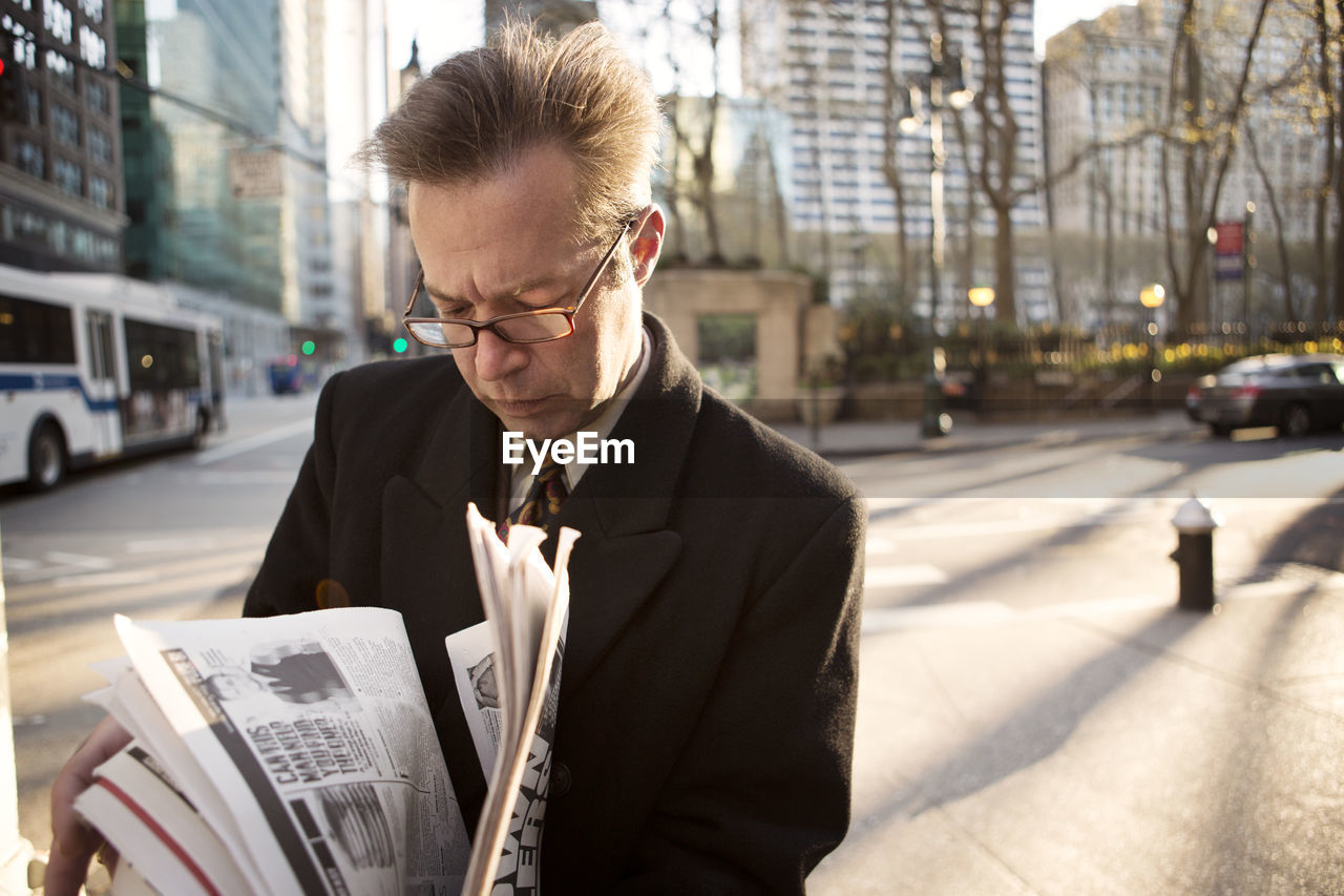 Businessman reading newspaper while standing on footpath