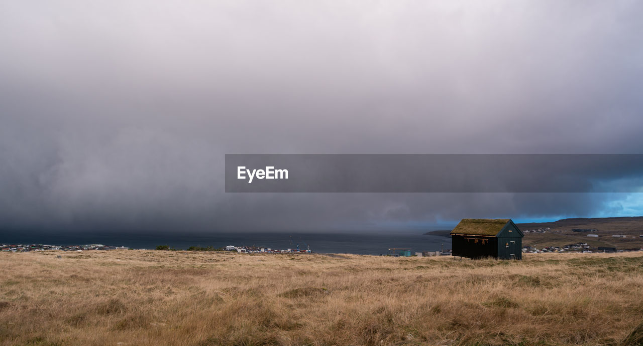 Scenic view of field by sea against storm clouds