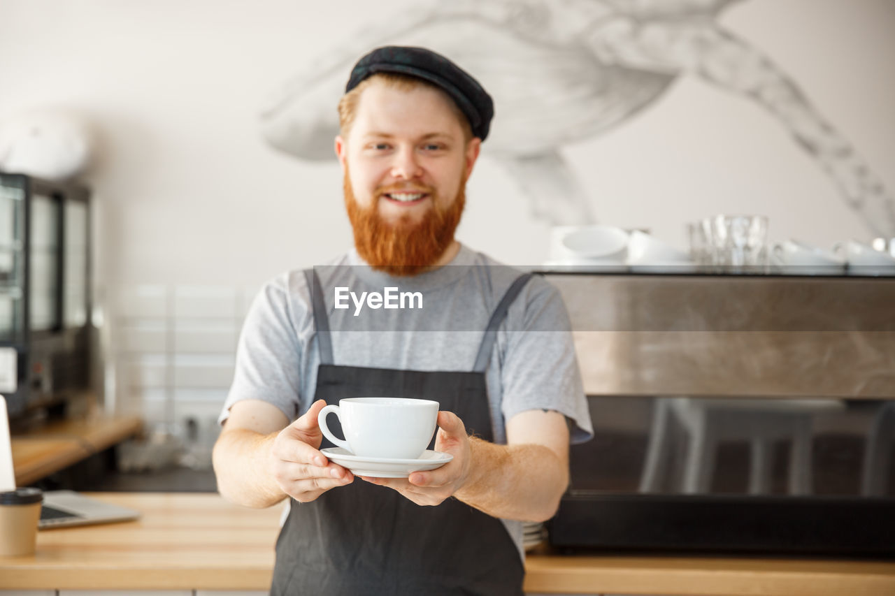 PORTRAIT OF SMILING MAN STANDING BY COFFEE