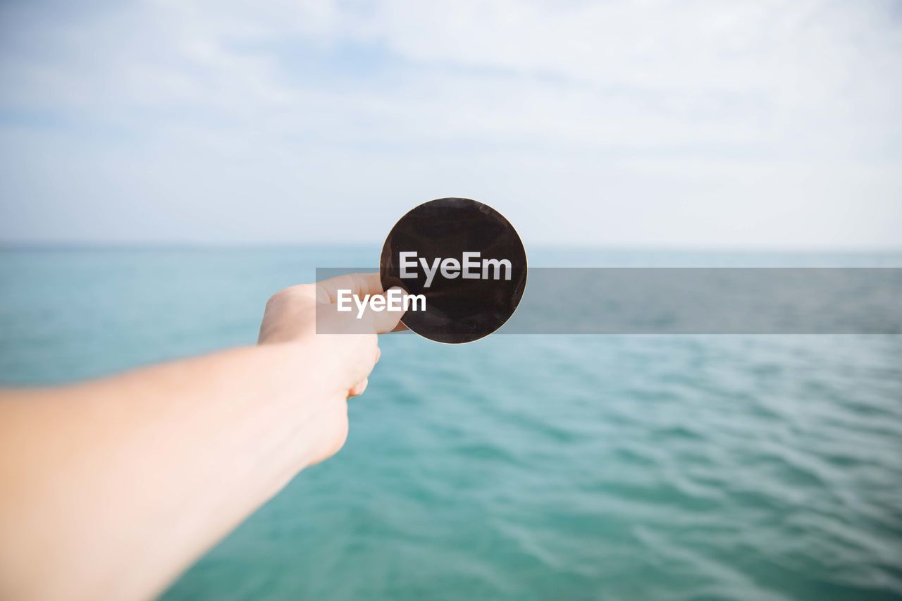 Cropped image of hand holding eyeem label against sea