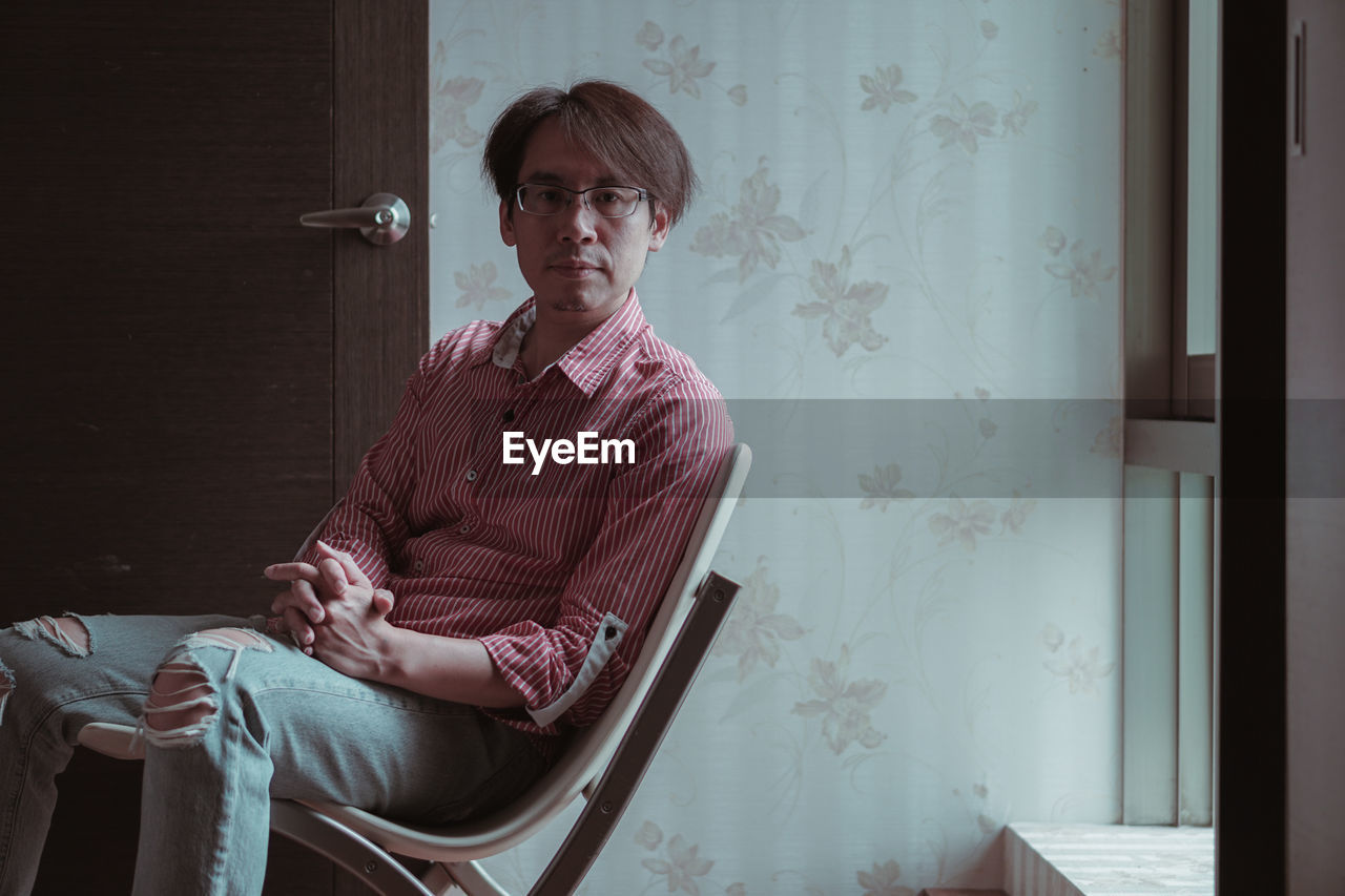 Young man looking away while sitting on chair at home