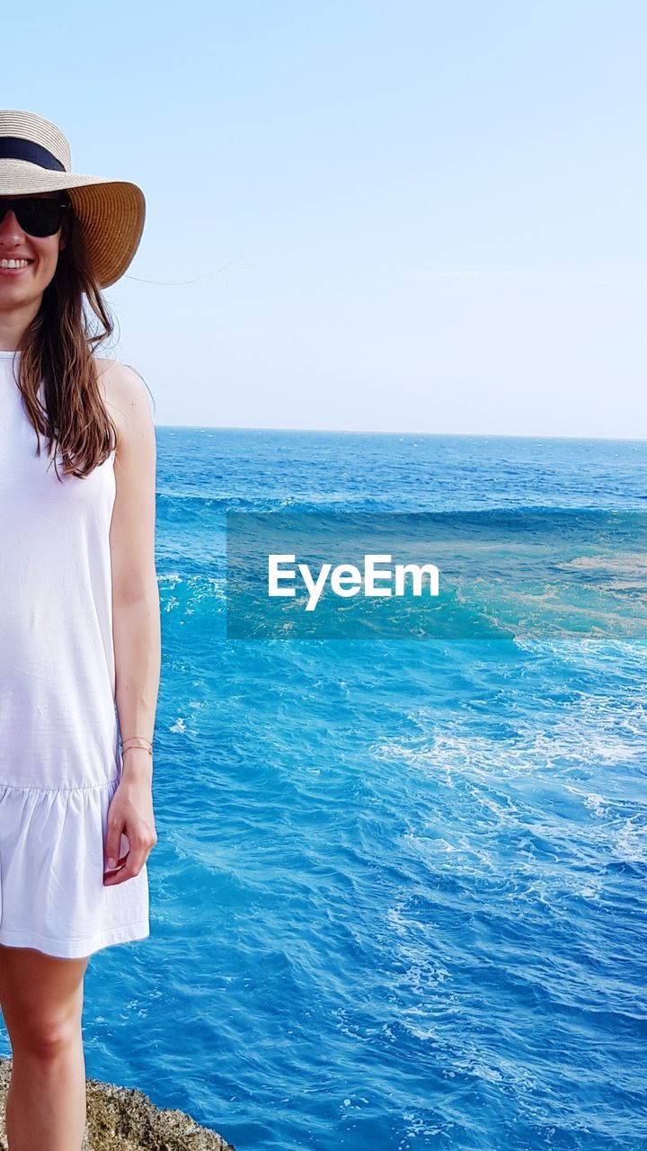 Portrait of young woman standing by sea against clear sky