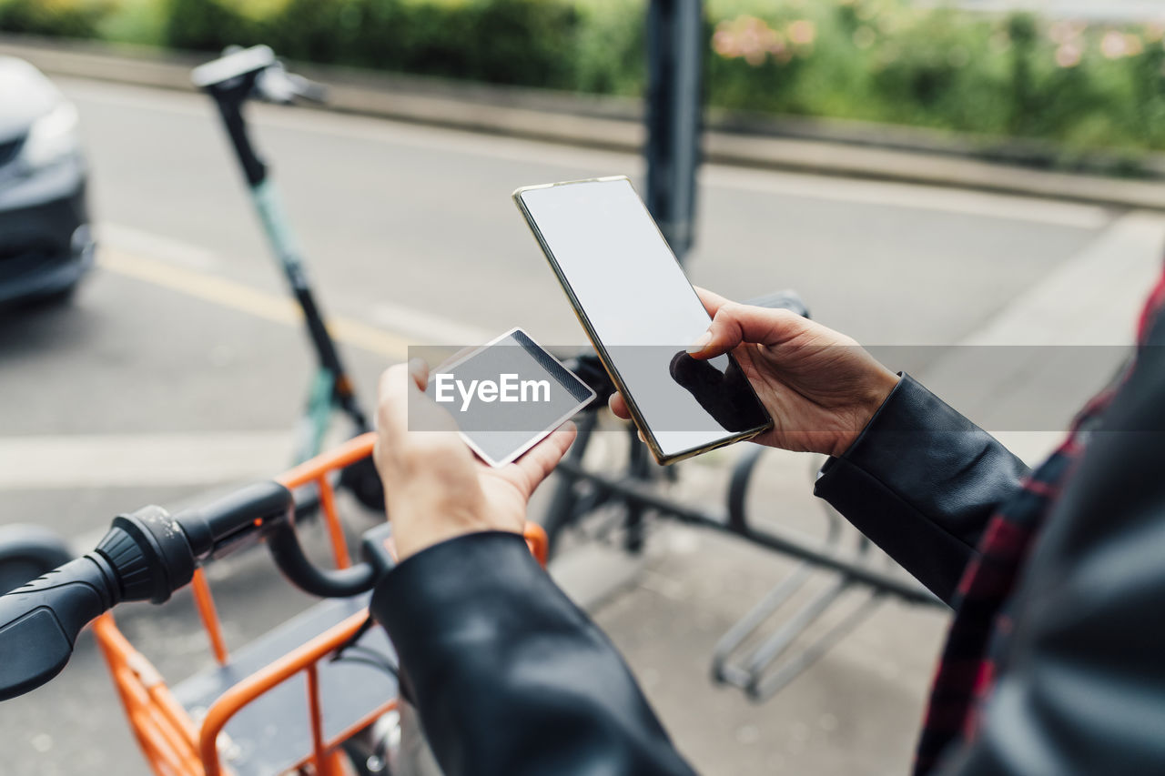 Woman with credit card using smart phone at bicycle parking station