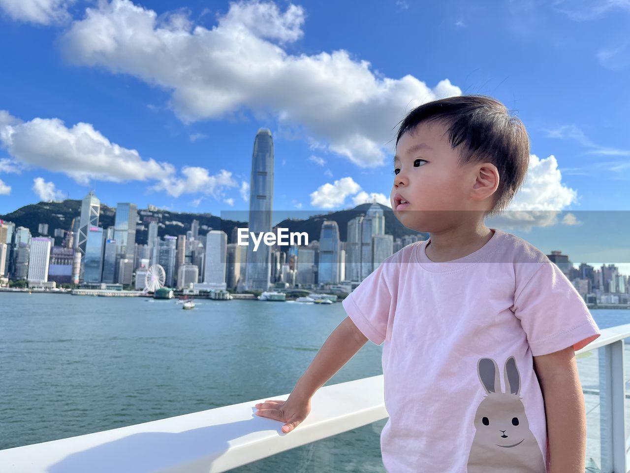 vacation, architecture, childhood, sky, one person, child, water, city, built structure, building exterior, cloud, nature, men, building, urban skyline, ship, standing, day, looking, travel destinations, portrait, waist up, casual clothing, outdoors, sea, lifestyles, leisure activity, nautical vessel, office building exterior, travel, cityscape, trip, transportation, skyscraper, holiday, smiling, looking away, landscape, blue, vehicle, sunlight, cute