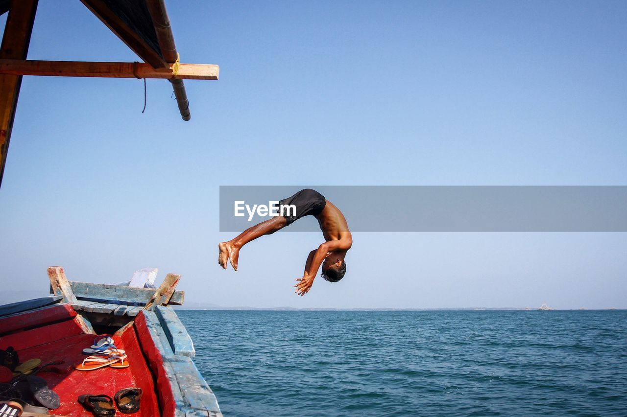 Man jumping from boat into sea against clear sky