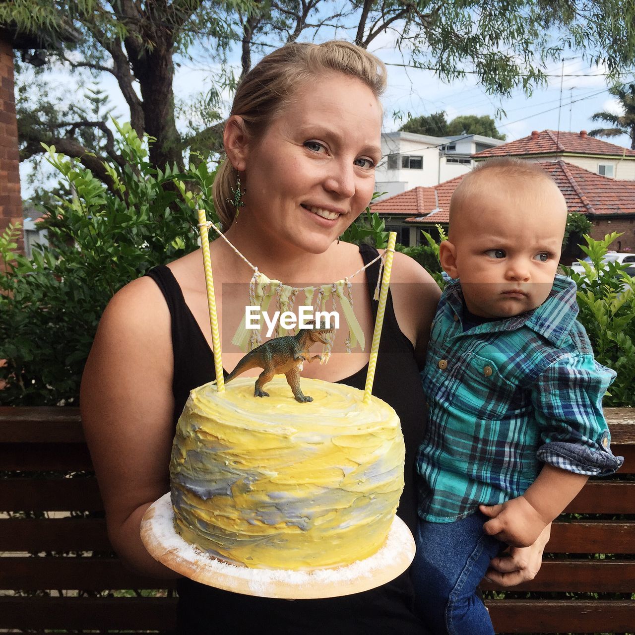 Portrait of smiling mother with cute son holding cake while crouching against plants