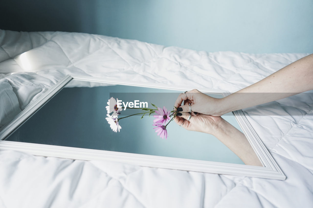 Hand of young woman leaving daisies on mirror lying on white duvet