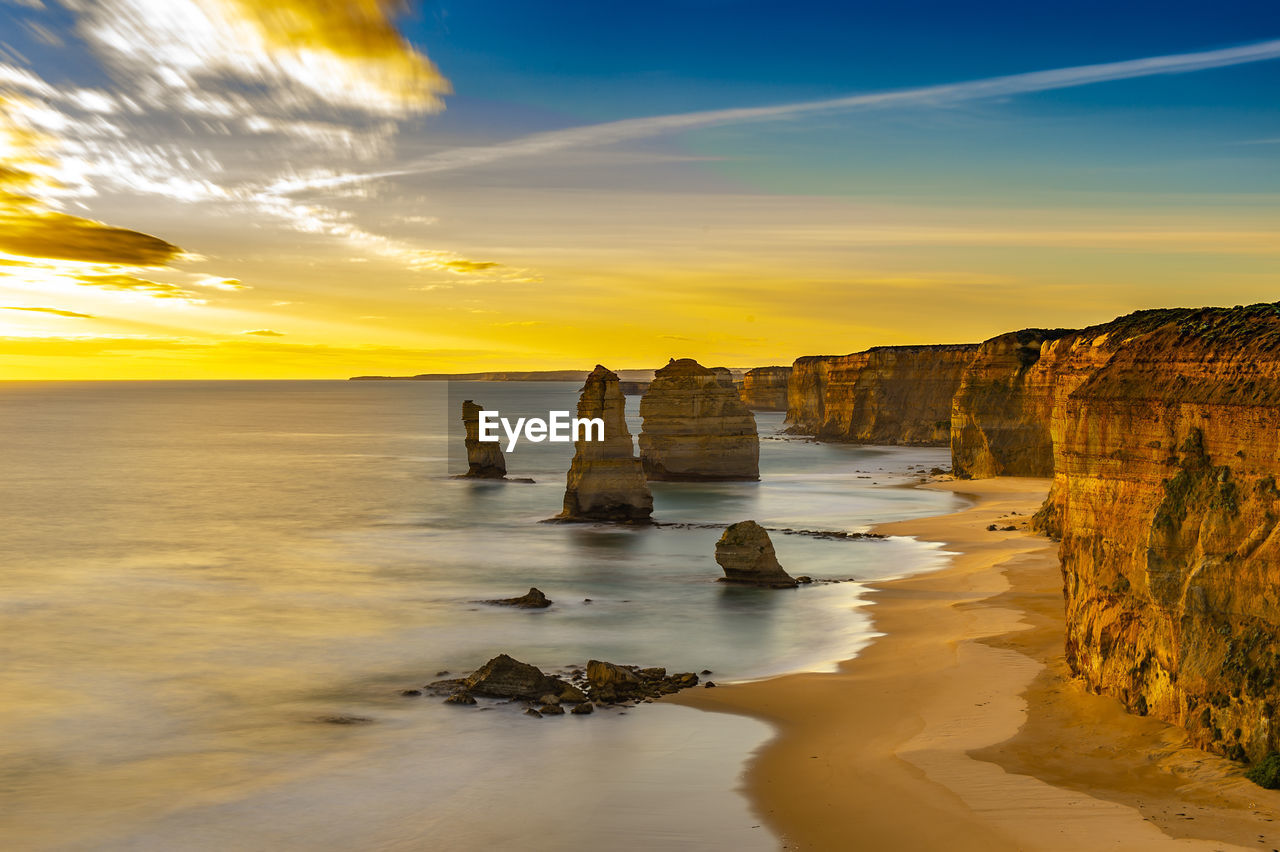 Scenic view of sea with rock formations at beach against sky during sunset