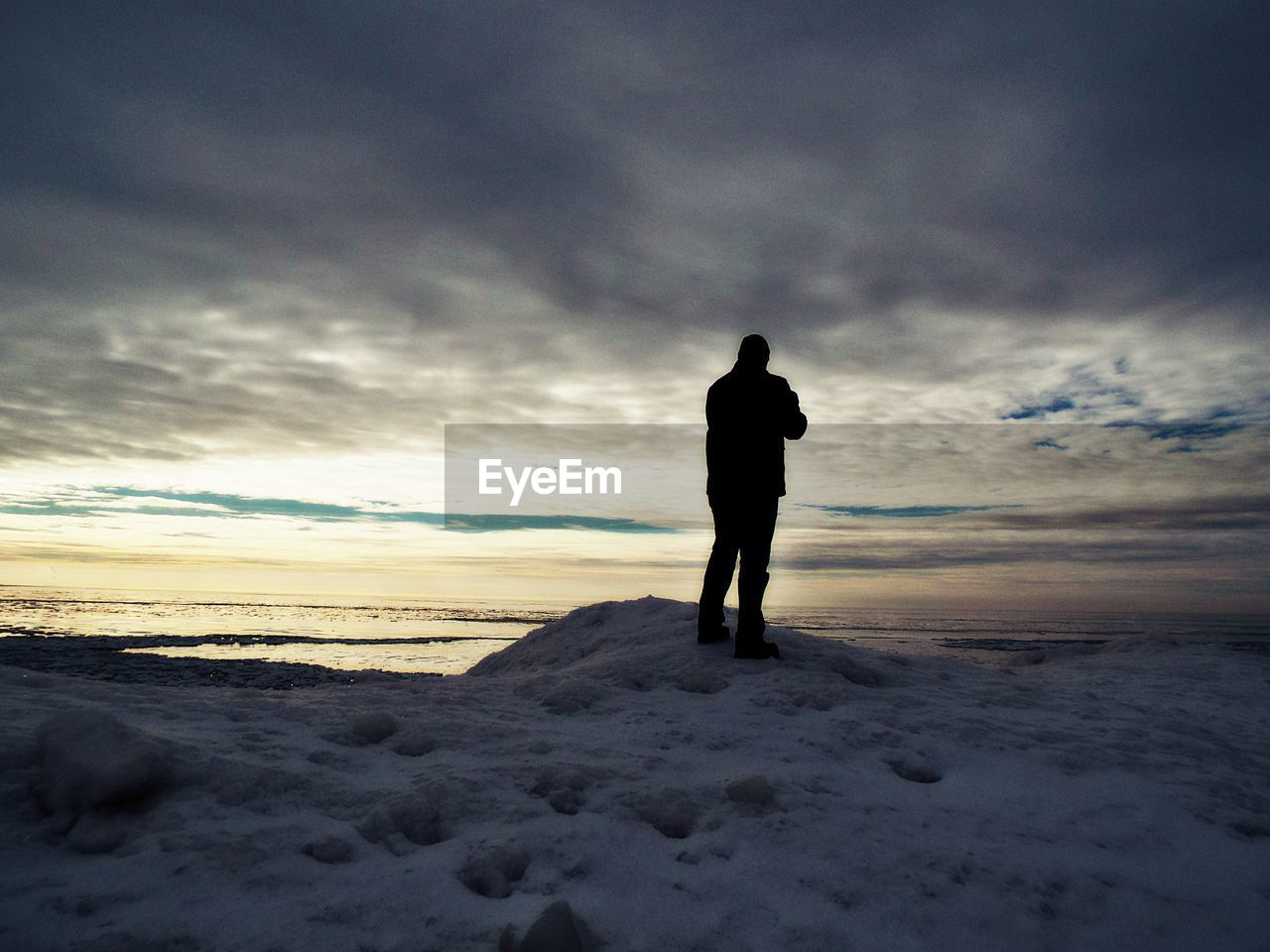 SILHOUETTE MAN STANDING ON BEACH AGAINST SKY DURING WINTER