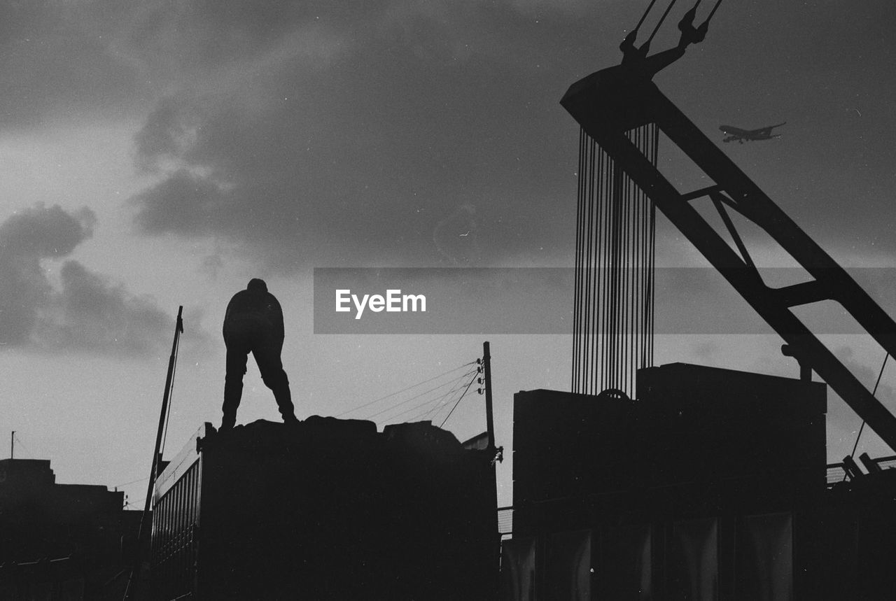 Low angle view of silhouette person standing by building against sky