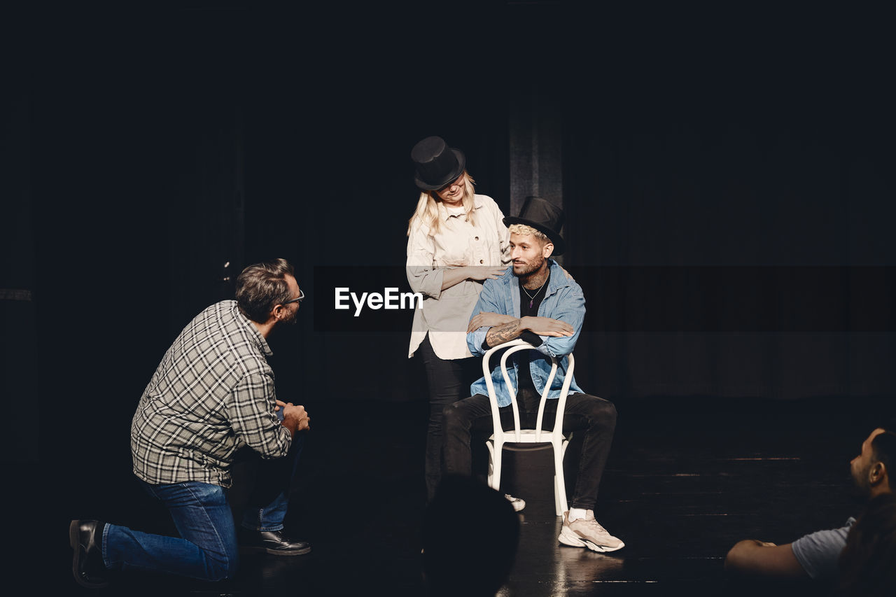 Instructor looking at man and woman wearing hat rehearsing on stage