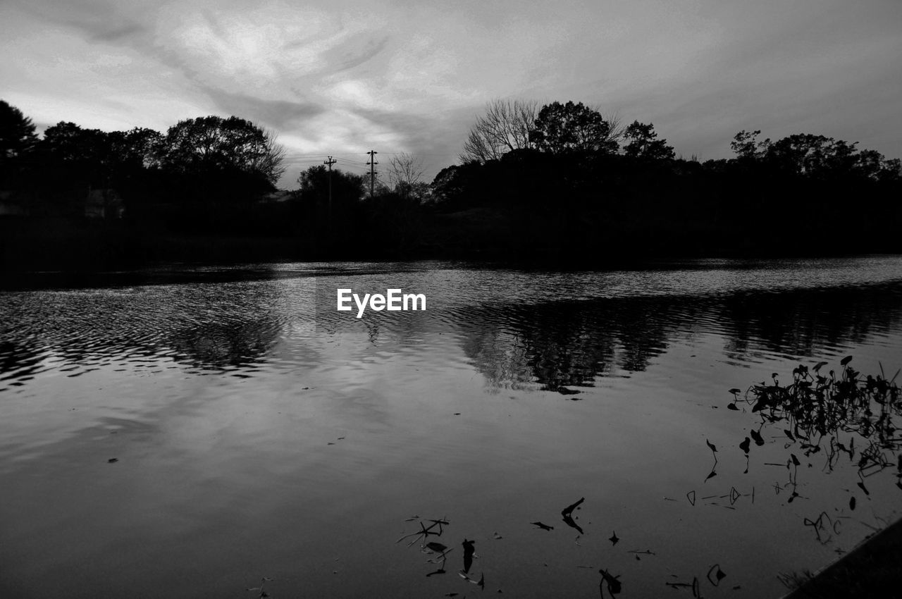 Silhouette trees by lake against sky