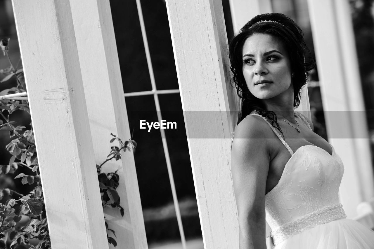 PORTRAIT OF BEAUTIFUL WOMAN STANDING BY WINDOW