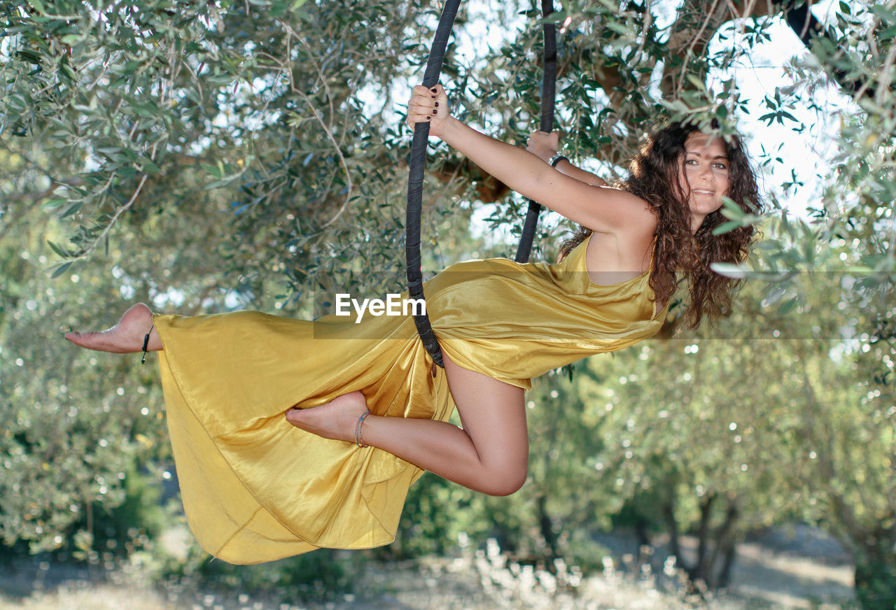 Young gymnast woman posing on a aeriel circle in fron of the olive trees garden