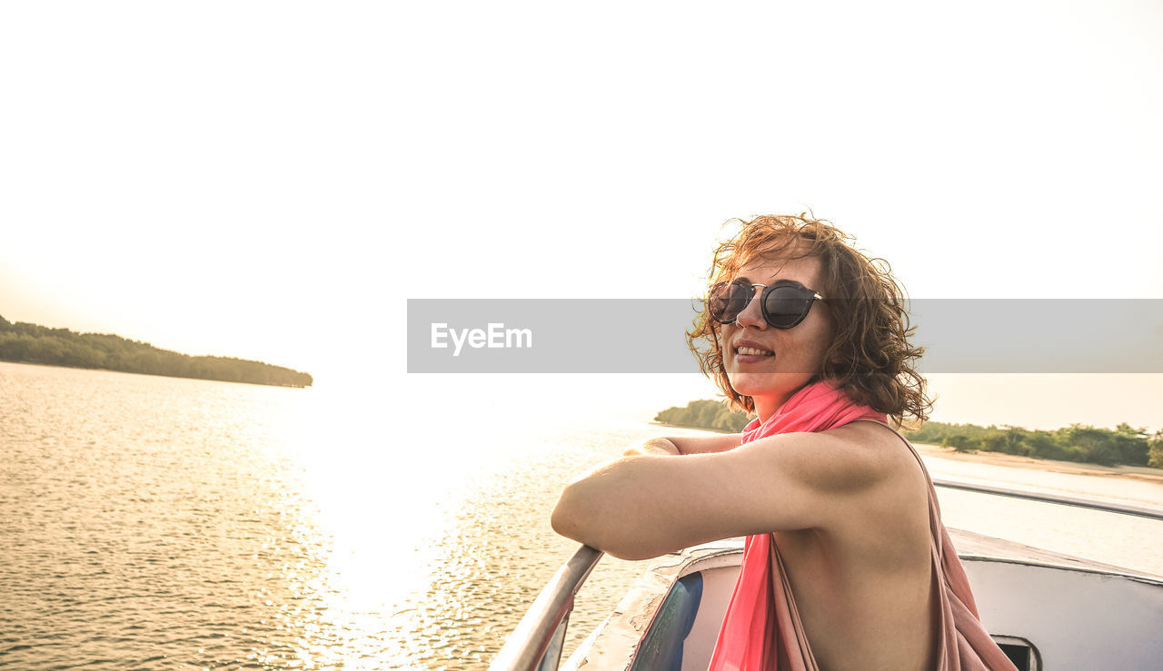 Woman in sunglasses standing at beach against sky