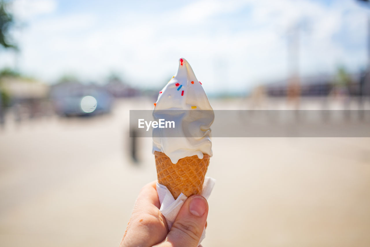 Female hand holds an ice cream cone on a street. ice cream melted and ran down fingers and hand.