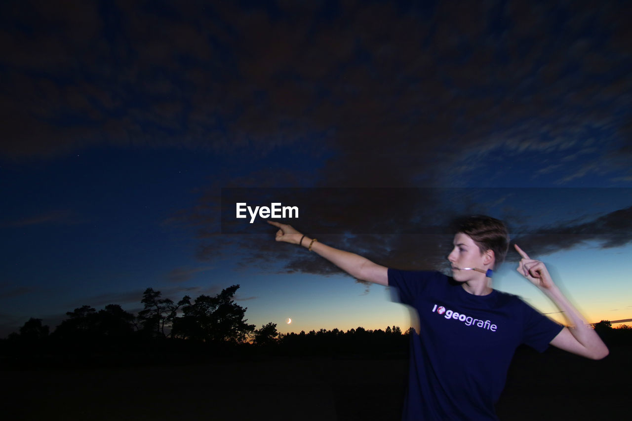 MAN STANDING IN FRONT OF TREES AGAINST SKY