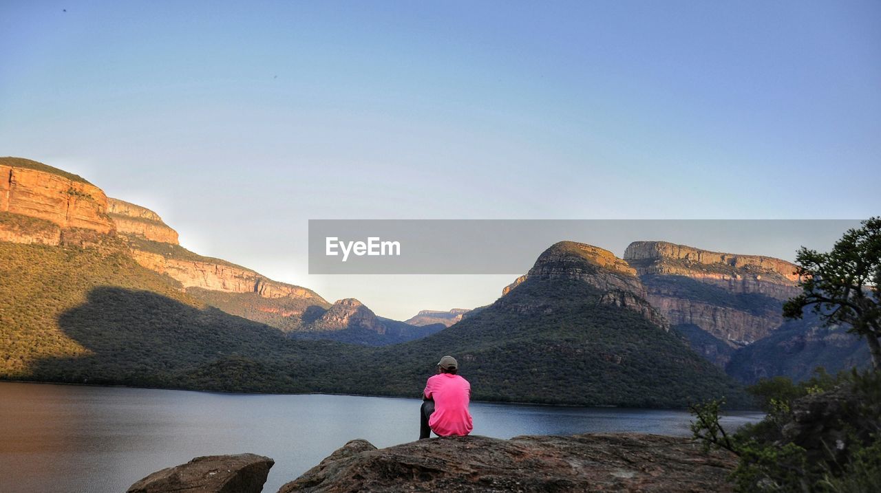 Man looking at lake and mountains against clear sky