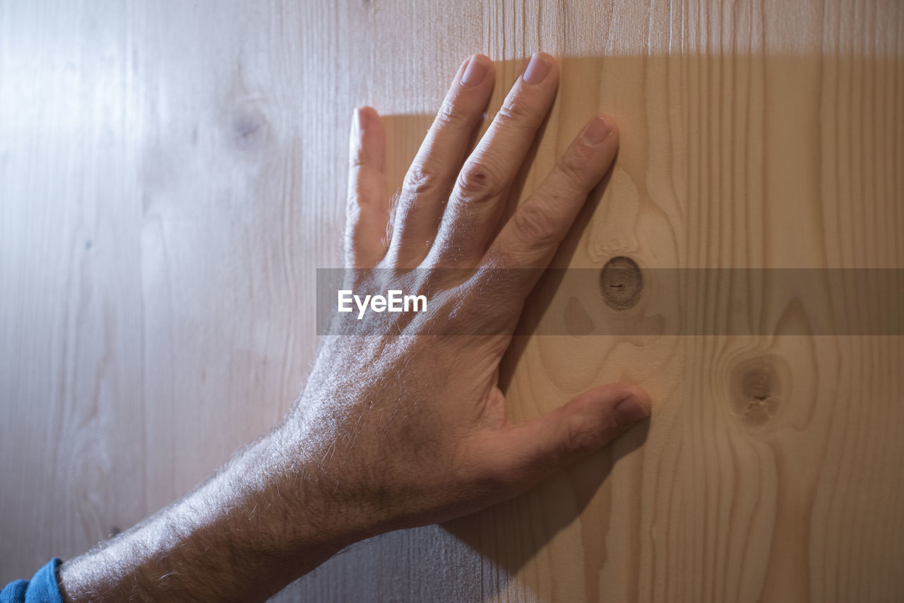 CLOSE-UP OF HUMAN HAND ON FLOOR AGAINST WALL