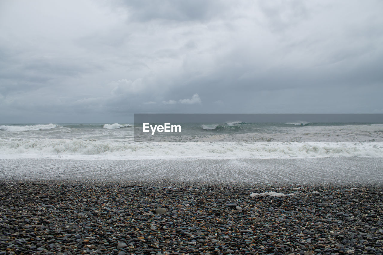 sea, land, water, beach, sky, horizon, cloud, shore, beauty in nature, ocean, wave, sand, wind wave, nature, scenics - nature, horizon over water, coast, body of water, motion, storm, tranquility, no people, day, environment, rock, outdoors, water sports, tranquil scene, sports, overcast, pebble, dramatic sky, storm cloud, seascape, idyllic, travel destinations, wind, sunlight