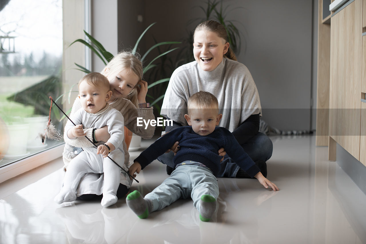 Mother with her three children playing with a cat on the floor at home