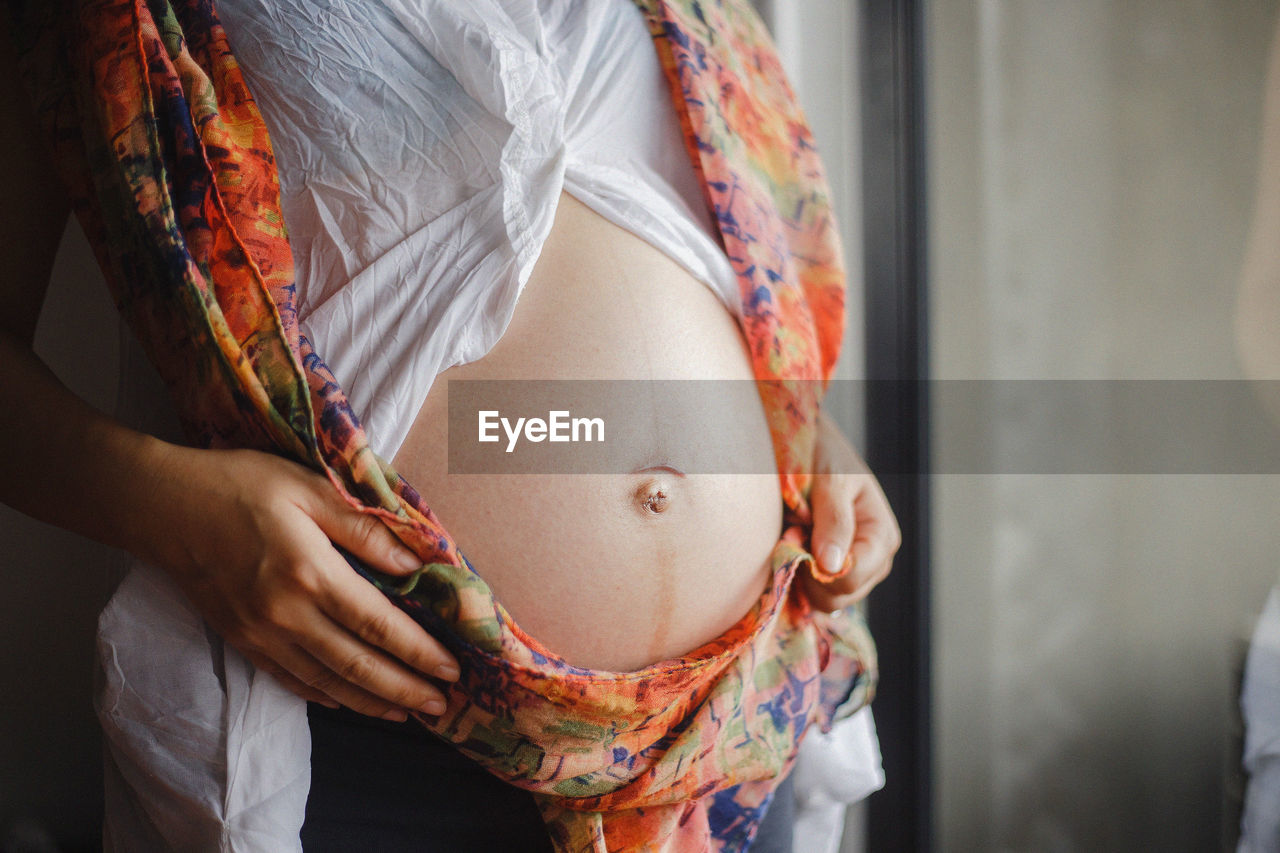 Midsection of pregnant woman standing at home