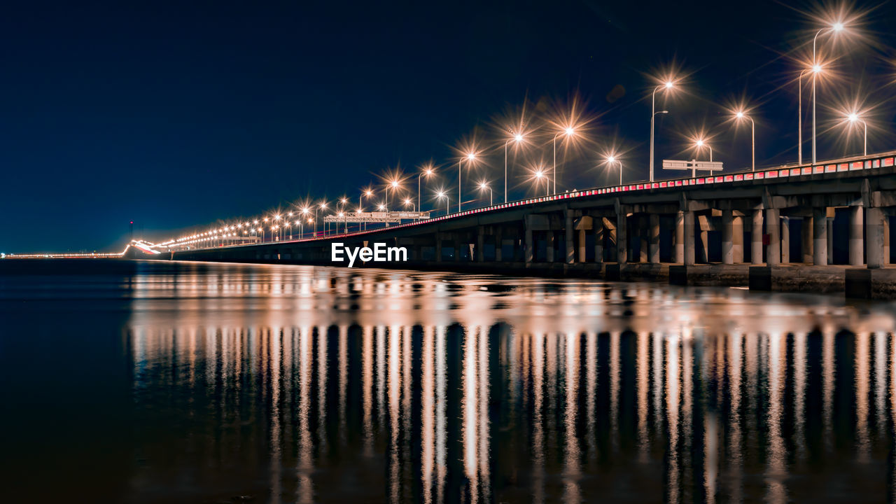 Illuminated bridge over river against sky at night