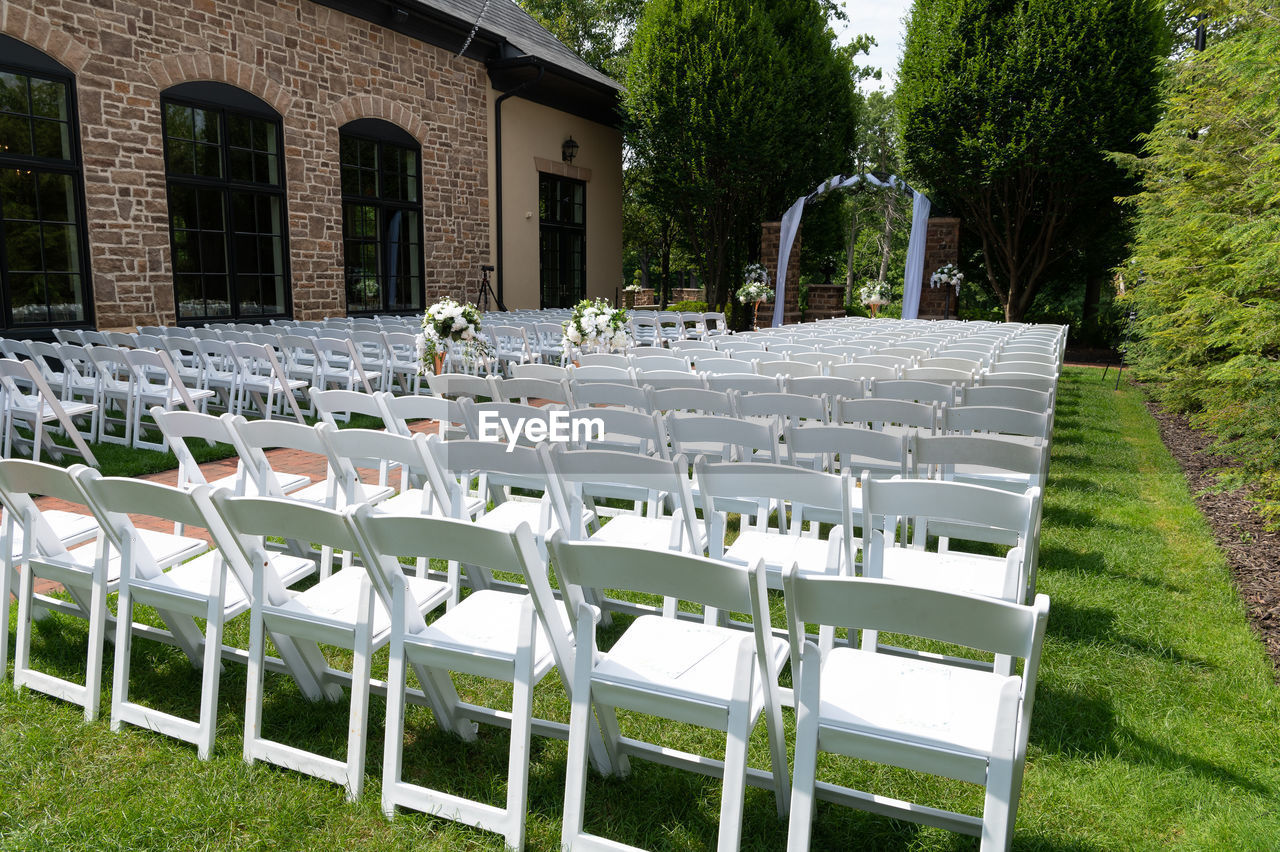 Outdoor wedding set up with white chairs in a garden.