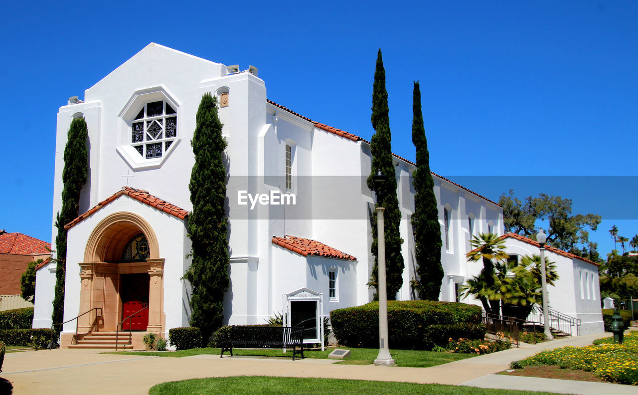 architecture, building exterior, built structure, building, sky, nature, plant, blue, clear sky, grass, estate, house, sunny, religion, no people, place of worship, entrance, tree, residential district, front or back yard, travel destinations, lawn, day, belief, outdoors, landmark, neighbourhood, sunlight